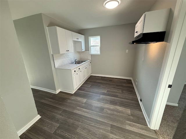 kitchen with a sink, dark wood finished floors, under cabinet range hood, light countertops, and baseboards