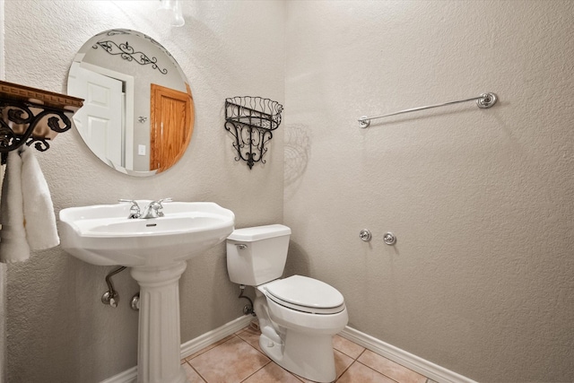 half bath featuring tile patterned flooring, toilet, and baseboards