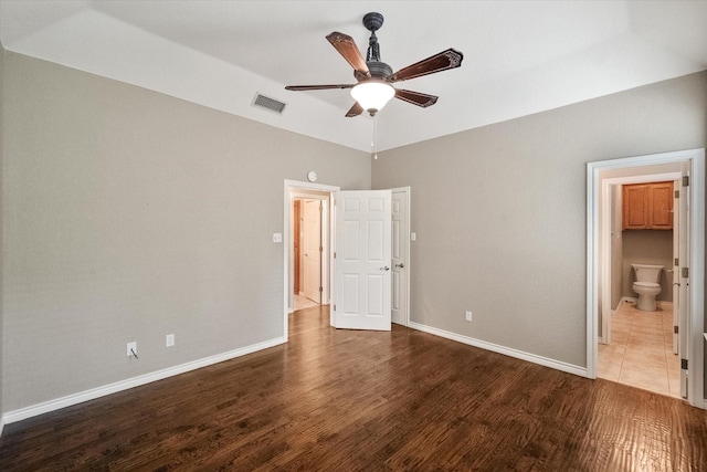 unfurnished bedroom featuring a ceiling fan, baseboards, ensuite bathroom, visible vents, and wood finished floors
