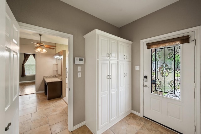 foyer entrance with baseboards, a ceiling fan, and stone tile floors
