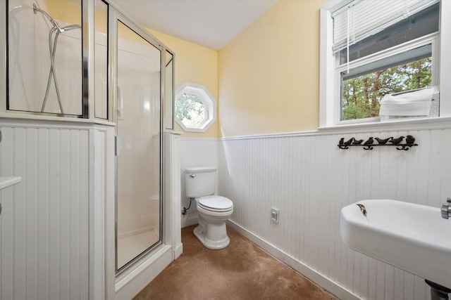 bathroom featuring a sink, toilet, concrete flooring, a shower stall, and wainscoting