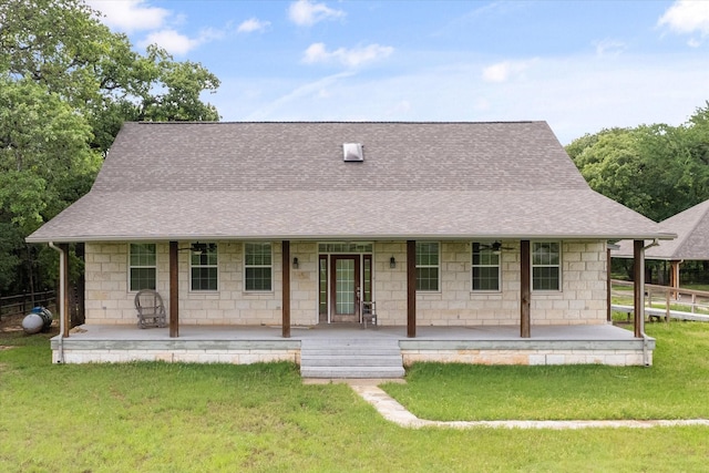 view of front of home featuring covered porch, stone siding, a front lawn, and a shingled roof