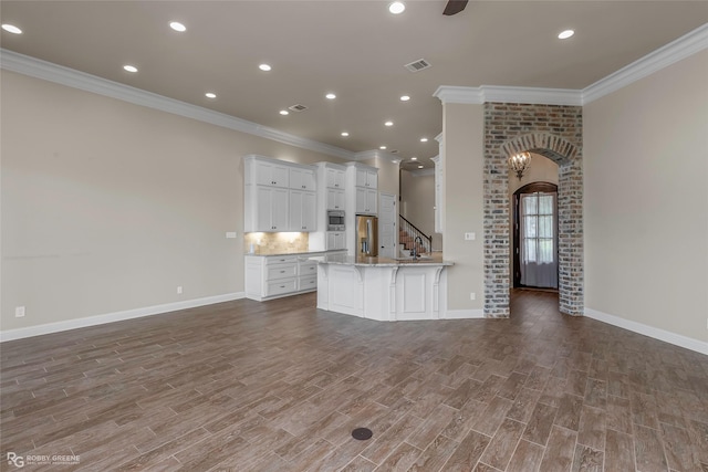 unfurnished living room featuring arched walkways, baseboards, visible vents, and crown molding