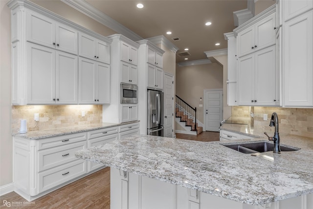 kitchen with a peninsula, a sink, white cabinets, crown molding, and appliances with stainless steel finishes