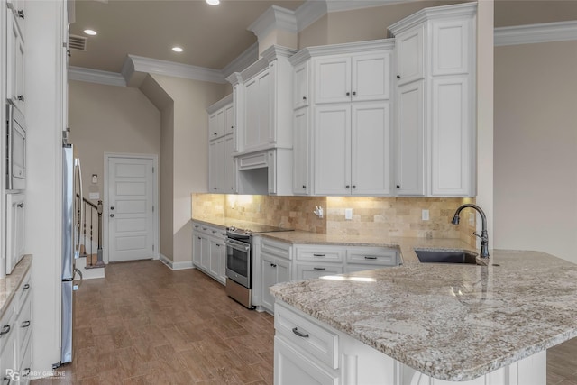 kitchen with a peninsula, appliances with stainless steel finishes, ornamental molding, and a sink