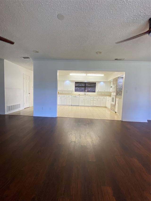 unfurnished room with a sink, a textured ceiling, visible vents, light wood finished floors, and baseboards