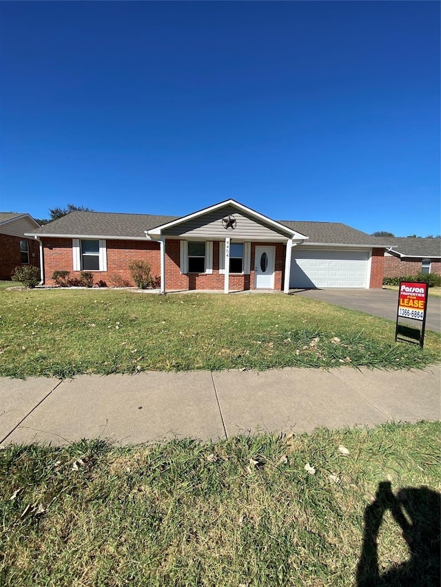 single story home with a front yard, brick siding, a garage, and driveway