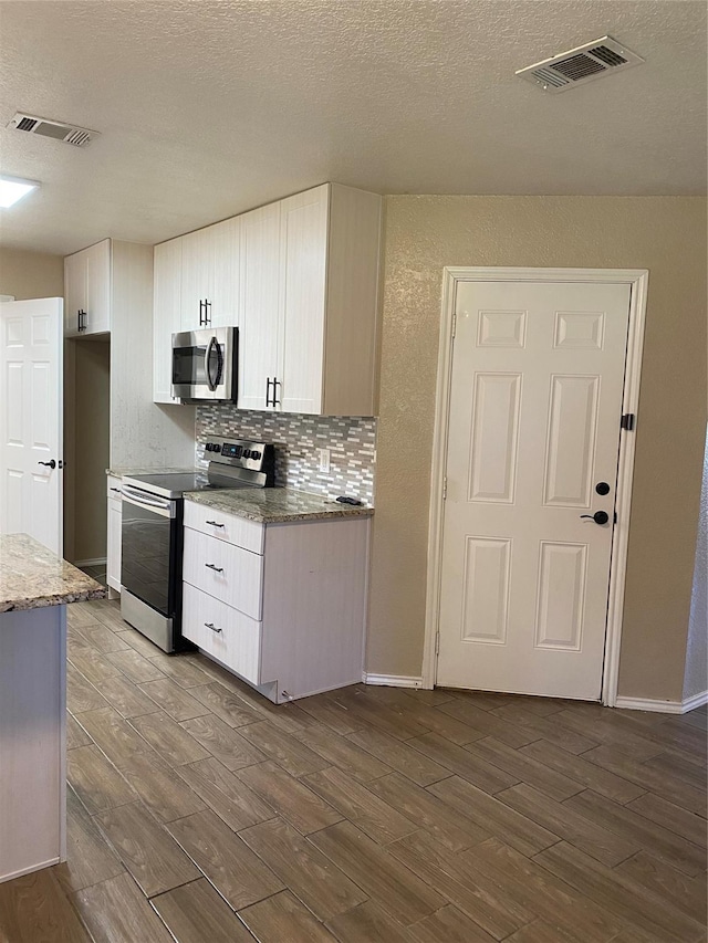 kitchen featuring dark wood-style flooring, stainless steel appliances, white cabinetry, and visible vents