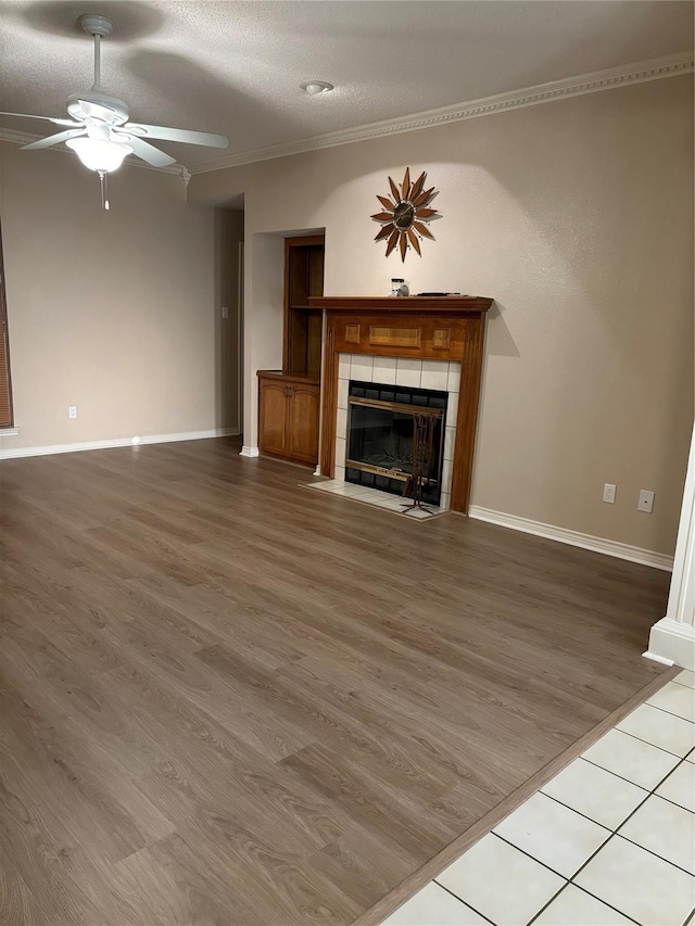 unfurnished living room with ceiling fan, baseboards, a tiled fireplace, and wood finished floors