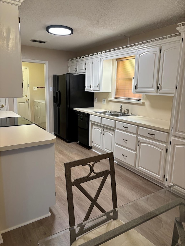 kitchen featuring washer and clothes dryer, a sink, a textured ceiling, light wood-type flooring, and black appliances