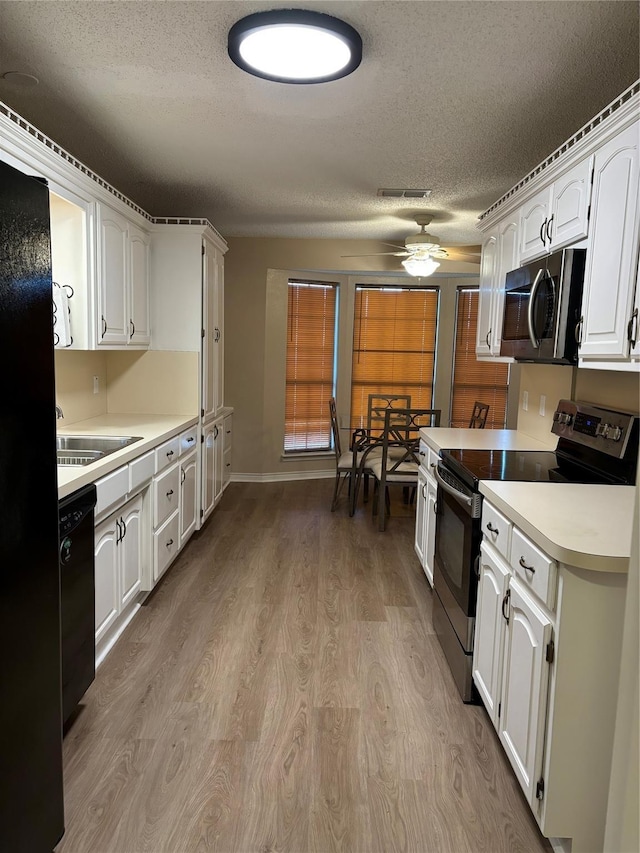 kitchen with white cabinets, light wood-style floors, appliances with stainless steel finishes, and a textured ceiling