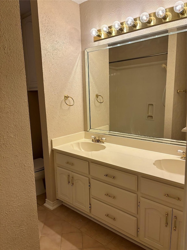 full bathroom featuring double vanity, tile patterned flooring, a sink, and a textured wall
