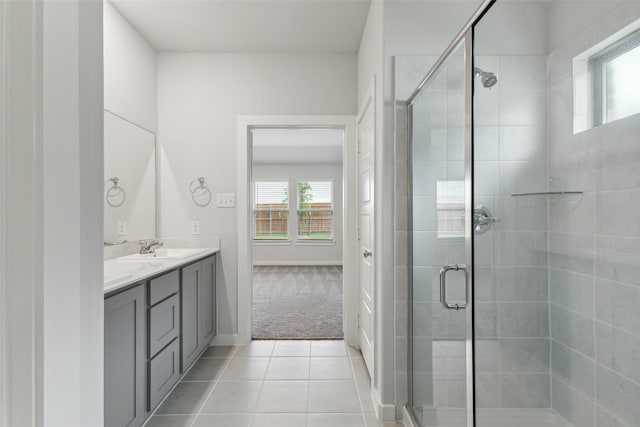 bathroom featuring a stall shower, baseboards, a sink, tile patterned floors, and double vanity