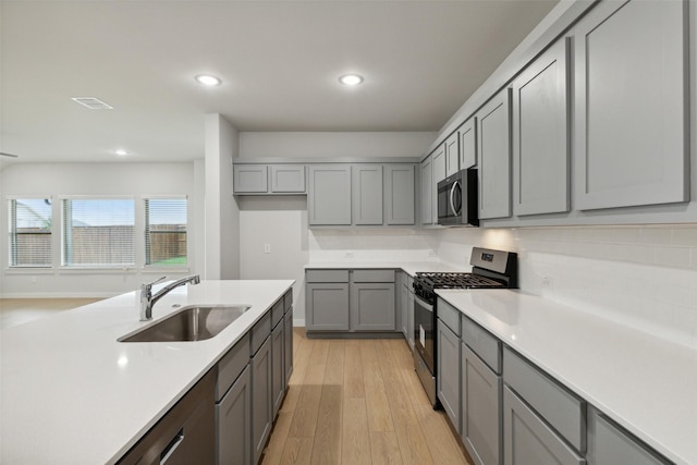 kitchen featuring gray cabinetry, appliances with stainless steel finishes, light wood-style floors, and a sink
