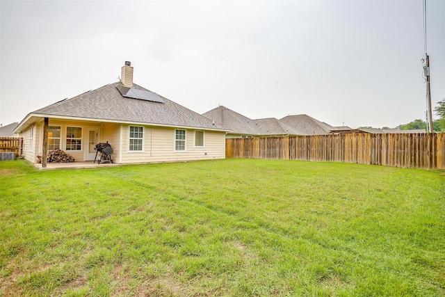 rear view of house with roof mounted solar panels, a chimney, a lawn, and a fenced backyard