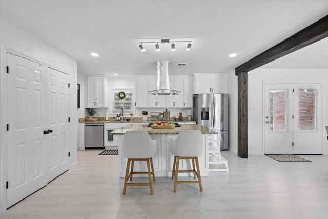 1718 Heather Rd, Gainesville, TX 76240 - kitchen featuring wall chimney exhaust hood, appliances with stainless steel finishes, a kitchen bar, a kitchen island, and white cabinets