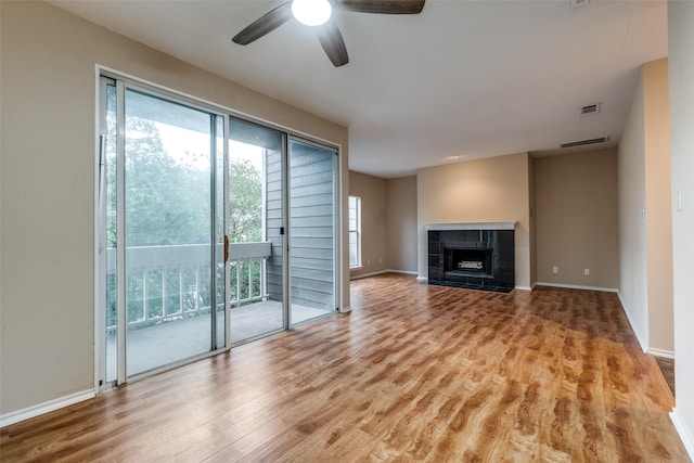 unfurnished living room featuring ceiling fan, a tile fireplace, plenty of natural light, and wood finished floors