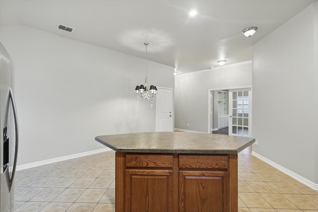 kitchen with light tile patterned floors, a center island, stainless steel fridge, brown cabinets, and a chandelier