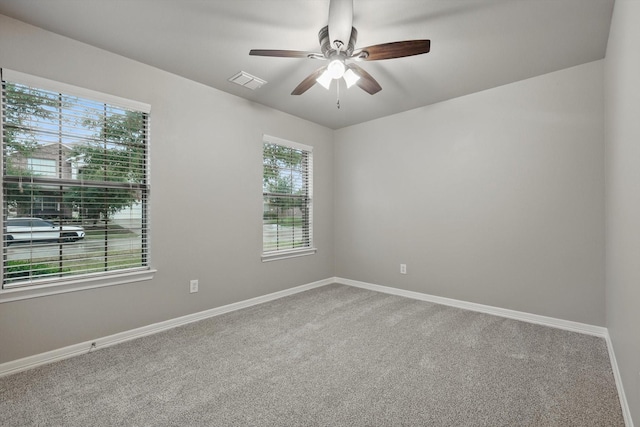 carpeted spare room with ceiling fan, visible vents, baseboards, and a healthy amount of sunlight