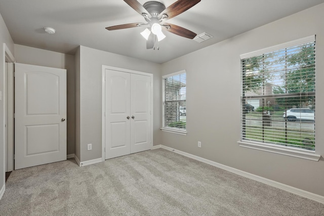 unfurnished bedroom with a closet, light colored carpet, visible vents, ceiling fan, and baseboards
