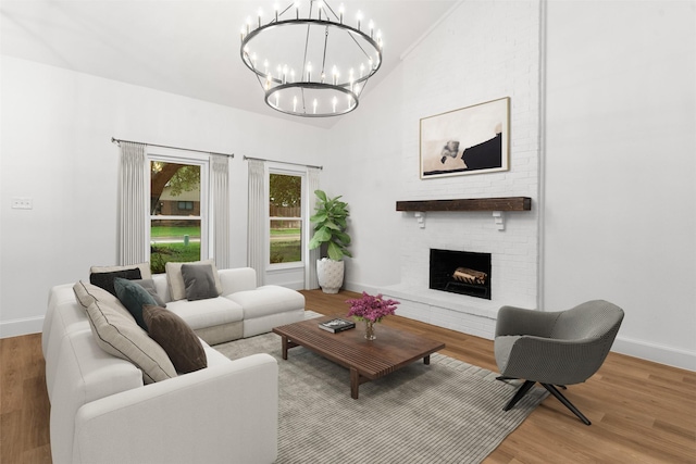 living room featuring vaulted ceiling, an inviting chandelier, a brick fireplace, and wood finished floors
