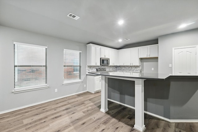 kitchen featuring light wood finished floors, decorative backsplash, visible vents, and stainless steel microwave