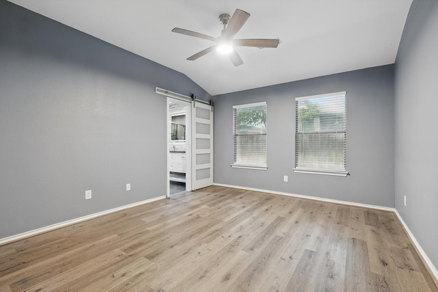 spare room featuring a ceiling fan, baseboards, a barn door, light wood-style floors, and lofted ceiling