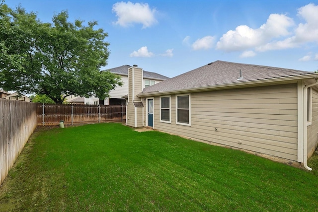 back of house with a shingled roof, a yard, and a fenced backyard