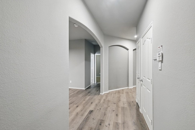 corridor featuring arched walkways, baseboards, a textured wall, and wood finished floors