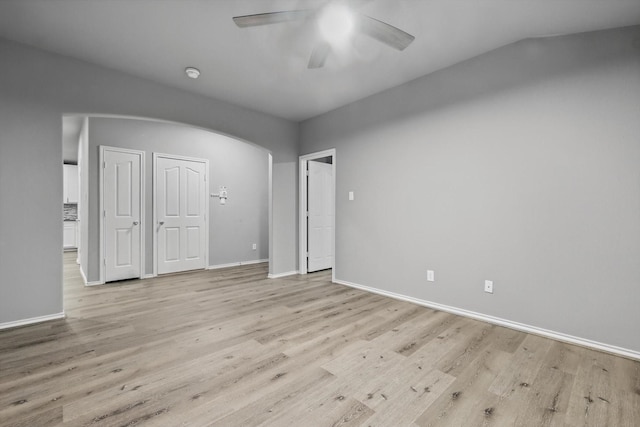 empty room with a ceiling fan, baseboards, light wood-style flooring, and arched walkways
