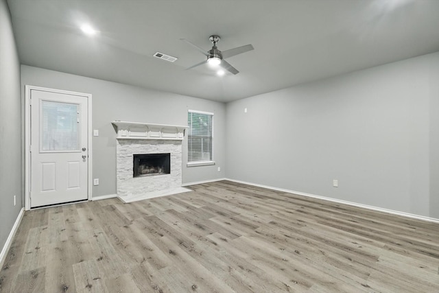 unfurnished living room with wood finished floors, visible vents, ceiling fan, baseboards, and a stone fireplace