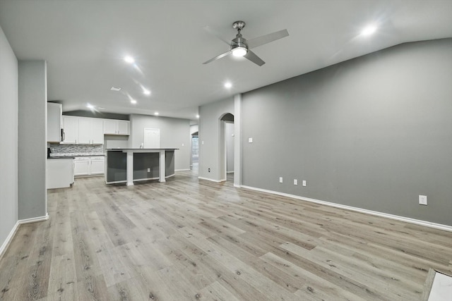 unfurnished living room with light wood finished floors, baseboards, a ceiling fan, and arched walkways