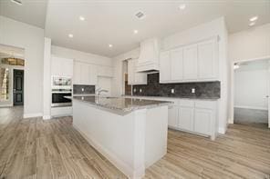 609 Alaina Dr, Desoto, TX 75115 - kitchen featuring light wood finished floors, double oven, white cabinetry, tasteful backsplash, and custom range hood