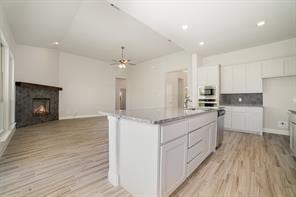 609 Alaina Dr, Desoto, TX 75115 - kitchen featuring a warm lit fireplace, ceiling fan, open floor plan, white cabinets, and light wood-style floors