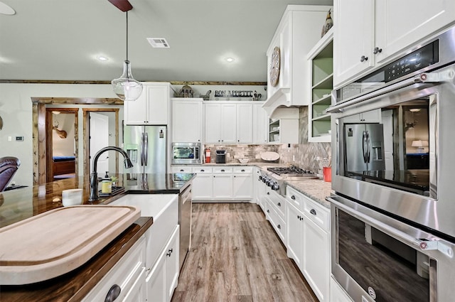 650 Scoggins Rd, Tioga, TX 76271 - kitchen with appliances with stainless steel finishes, decorative backsplash, white cabinets, pendant lighting, and light wood-style floors