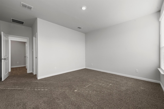 spare room featuring baseboards, dark carpet, and visible vents