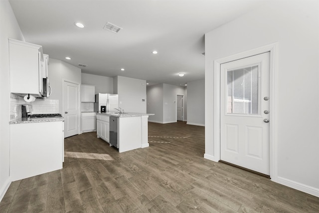kitchen with an island with sink, white cabinets, baseboards, appliances with stainless steel finishes, and dark wood-style floors