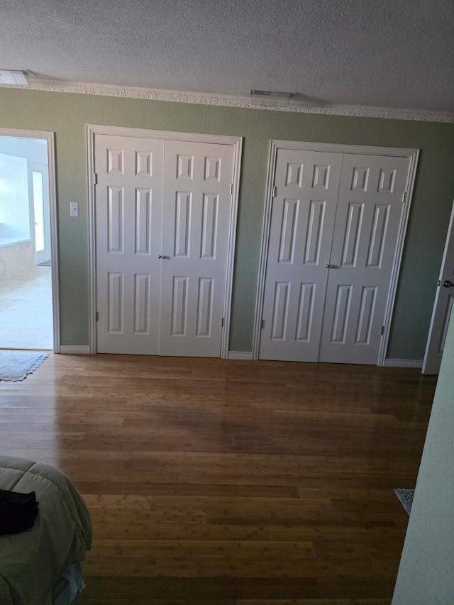 1608 University Dr, Richardson, TX 75081 - unfurnished bedroom featuring two closets, wood finished floors, a textured ceiling, and baseboards