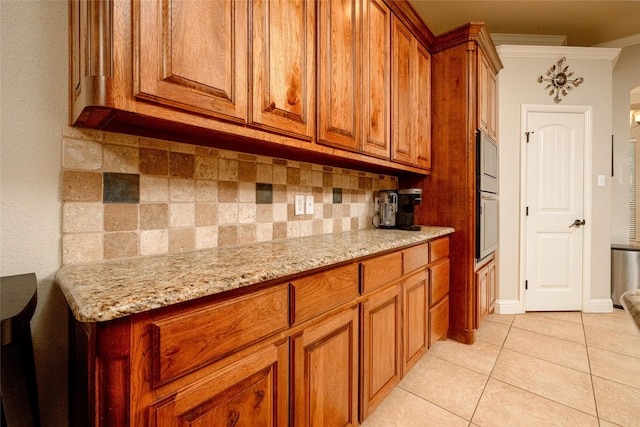 kitchen featuring light stone countertops, brown cabinetry, decorative backsplash, and light tile patterned floors