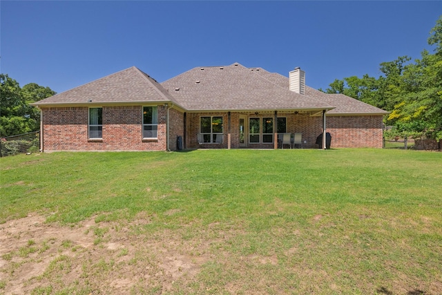 rear view of property featuring fence, a chimney, a yard, roof with shingles, and brick siding