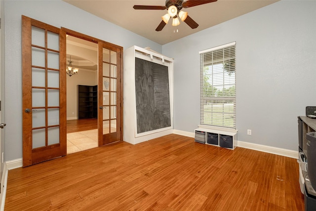 empty room with wood finished floors, french doors, baseboards, and ceiling fan with notable chandelier