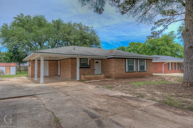 single story home featuring an outdoor structure, brick siding, driveway, a storage unit, and an attached carport