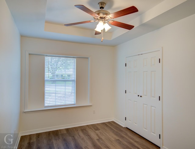spare room with a ceiling fan, baseboards, a tray ceiling, and wood finished floors