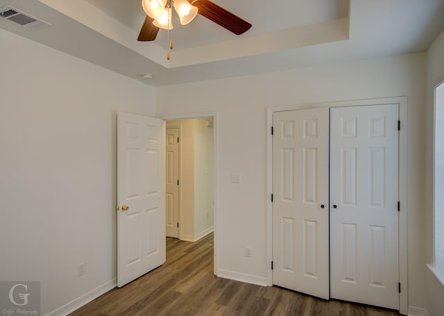 unfurnished bedroom featuring a tray ceiling, baseboards, dark wood-style floors, and visible vents