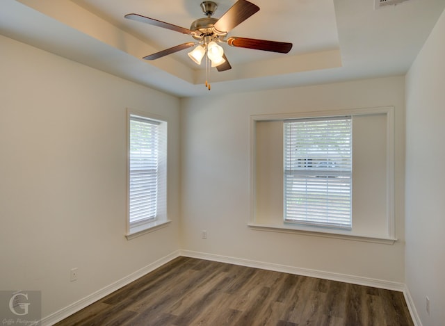 empty room featuring a raised ceiling, ceiling fan, and dark wood-style floors