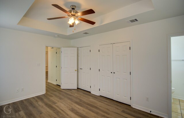 unfurnished bedroom featuring a raised ceiling, multiple closets, visible vents, and wood finished floors