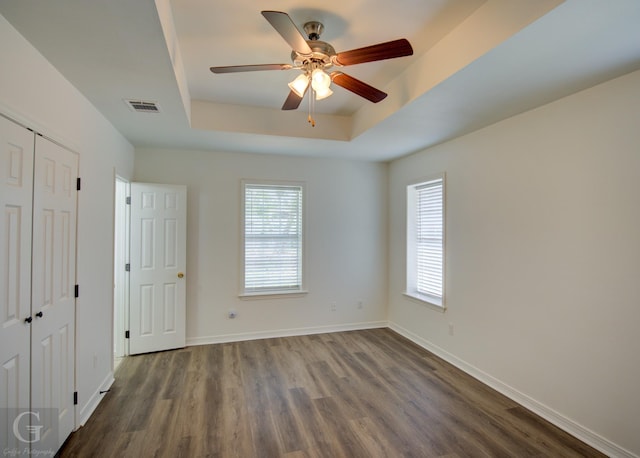 unfurnished bedroom featuring a tray ceiling, baseboards, dark wood-type flooring, and visible vents