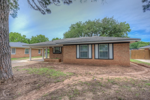 ranch-style home with fence, a shingled roof, a carport, and brick siding