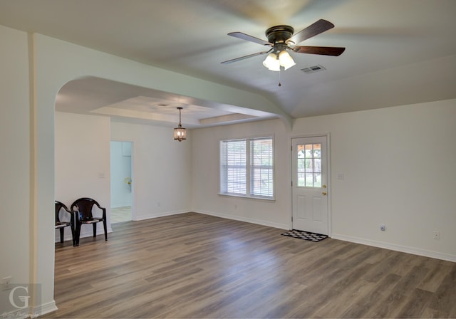 interior space featuring a ceiling fan, a tray ceiling, visible vents, wood finished floors, and arched walkways