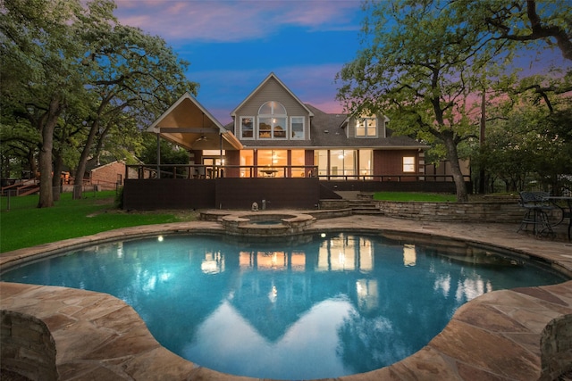 pool at dusk with a yard, ceiling fan, a pool with connected hot tub, a patio area, and a wooden deck